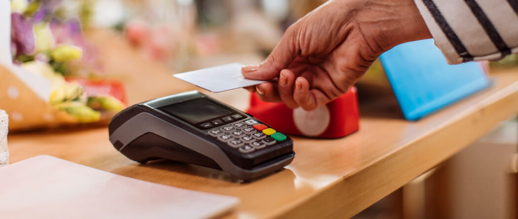 Close up of a person's hand holding a credit card up to a card reader